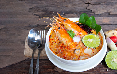 Tom Yum Goong or Shrimp soup spicy sour Soup Traditional food in Thailand contains chili, lime,lemongrass, lime leaf, along with cooked rice in a white dish on the old wood background.