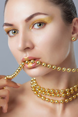 Portrait of a beautiful happy woman with beautiful creative makeup in gold colors. She has gold beads on her neck, in her hands and on her lips, and gold earrings. Make-up concept.