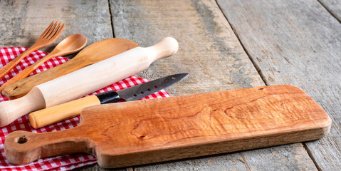 Kitchen utensil tools including cutting board, knife and spoons with rustic wooden background. Top...
