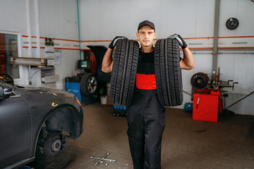 Fototapeta na wymiar Auto repairman holds two tires, repairing service