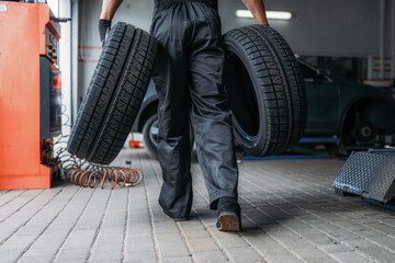 Obraz na płótnie Canvas Auto mechanic holds two tires, repairing service