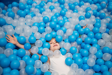 Happy baby in dry pool. Blue and white balls. Children's room.