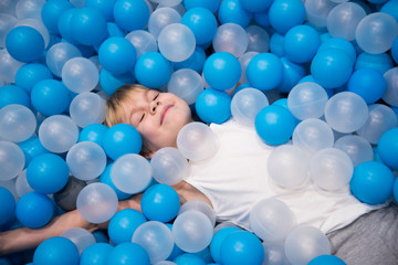 Fototapeta na wymiar Happy baby in dry pool. Blue and white balls. Children's room.