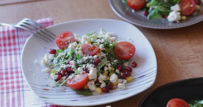 Fresh made arugula salad with cherry tomatoes, soft cheese, sweetcorn kernel and pomegranate seed on plate on rotating stand, close up