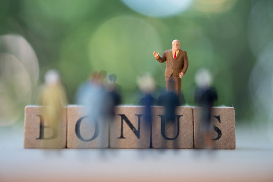 Miniature business man stand on block of words of bonus
