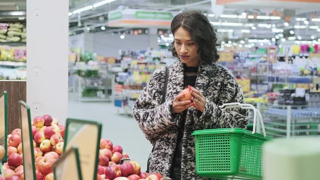 African american woman shopping apples from shelf in super market. Woman take red apple in marketplace. Medium shot of female choosing organic fruits in grocery store. 4K, UHD