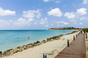 Beautiful view of white sand Aruba beach. Blue sunbeds under sun umbrellas on turquoise water and blue sky with white clouds background. Caribbean. Atlantic ocean. Aruba. 