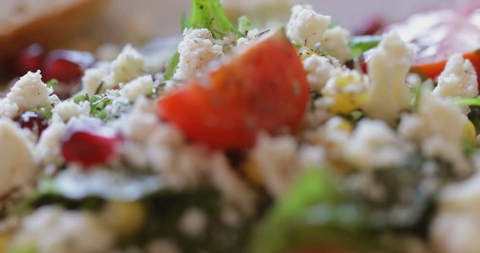 Fresh made arugula salad with cherry tomatoes, soft cheese, sweetcorn kernel and pomegranate seed on plate on rotating stand, close up