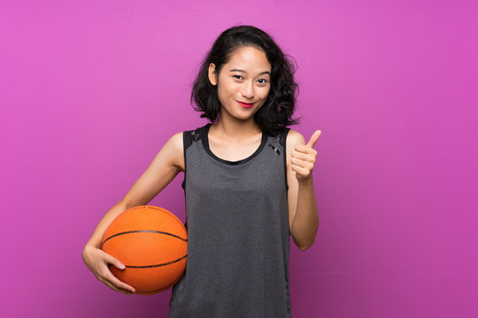 Young Asian woman playing basketball over isolated purple background
