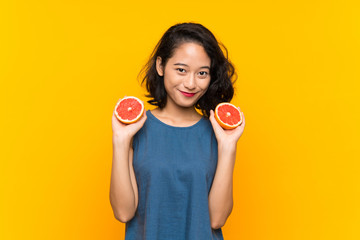 Young asian girl holding a grapefruit over isolated orange background