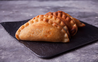 Mexican fried meat pies empanadas cheburek on the black plate on the concrete background