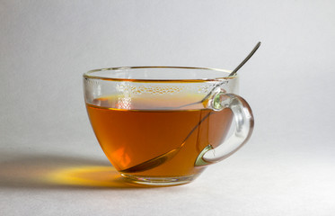 A cup of hot tea and a spoon on a light blurry background.