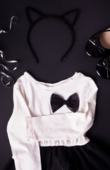 Black white dress with black bow, black shoes and hair band with cat's ears on the black background. Party fashion for girls.
