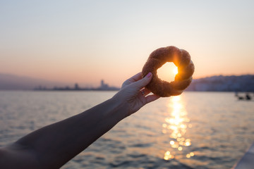 turkish bagel simit in womans hand at dawn against the backdrop of the gulf of Izmir