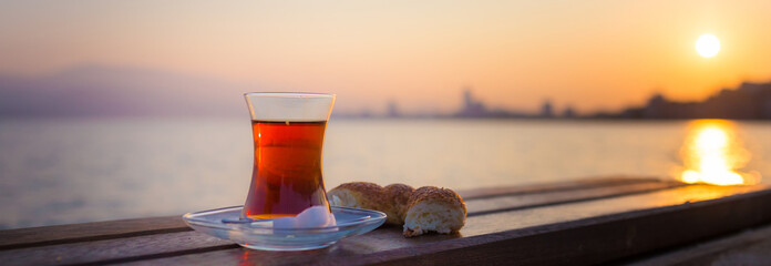 tea in traditional turkish glass and turkish bagel simit at dawn against the backdrop of the gulf of Izmir banner