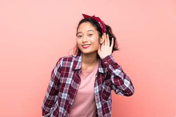 Asian young woman over isolated pink background listening to something by putting hand on the ear