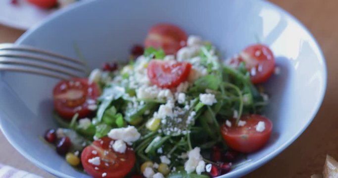 Fresh made arugula salad with cherry tomatoes, soft cheese, sweetcorn kernel and pomegranate seed on plate on rotating stand, close up