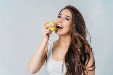 Beauty portrait of smiling young asian woman girl holding green apple near clean face on grey...