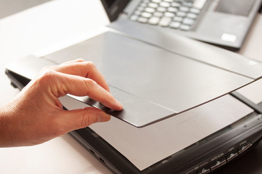 A hand closing a flatbed scanner with a laptop computer in the background. Selective focus image.