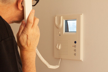 Man answering a call at a door phone while looking at the screen on the CRT display. Video intercom equipment. Selective focus image. - 308082480