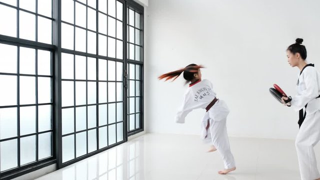 Taekwondo coach use kickpad or tools for training to her trainee in the gym with glass windows. The text show on belt and back of trainee mean taekwondo