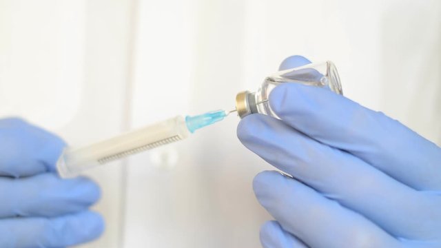 Doctor's hands with blue gloves fill the syringe with vaccine or insuline injection, preparing for the injection to the patient close-up