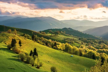 Fotobehang mountainous countryside at sunset. landscape with grassy rural fields and trees on hills rolling in to the distance in evening light. distant ridge and valley in haze. fantastic scenery in springtime © Pellinni