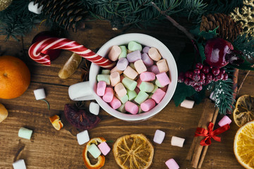 Christmas mug with marshmallows on a wooden background with Christmas toys. Caramel cane, tangerines and cinnamon.