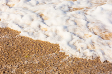 Fototapeta na wymiar sea waves splash foam on the sunny beach. mess of salt water and sand in evening light. dynamic nature texture