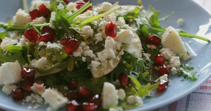 Fresh made arugula salad with cherry tomatoes, soft cheese, sweetcorn kernel and pomegranate seed on plate on rotating stand, close up