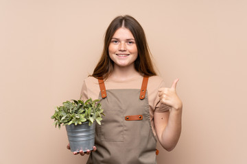 Ukrainian teenager gardener girl holding a plant giving a thumbs up gesture