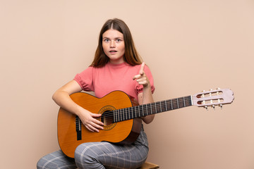 Fototapeta premium Ukrainian teenager girl with guitar over isolated background surprised and pointing front