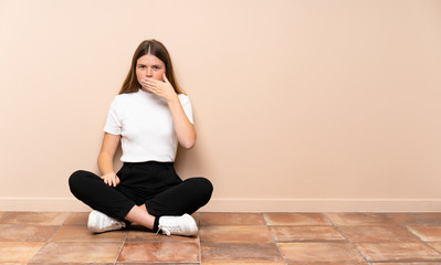 Ukrainian teenager girl sitting on the floor covering mouth with hands
