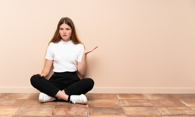 Ukrainian teenager girl sitting on the floor making doubts gesture
