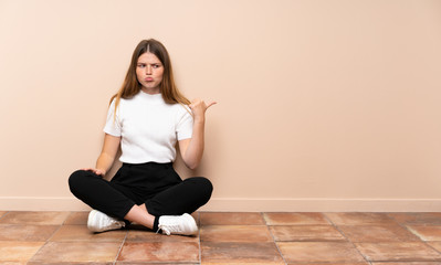 Fototapeta na wymiar Ukrainian teenager girl sitting on the floor unhappy and pointing to the side