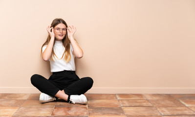 Fototapeta na wymiar Ukrainian teenager girl sitting on the floor with glasses and surprised