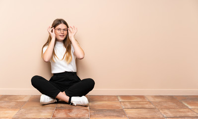 Fototapeta premium Ukrainian teenager girl sitting on the floor with glasses and surprised