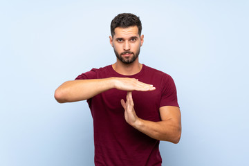 Handsome man over isolated blue background making time out gesture