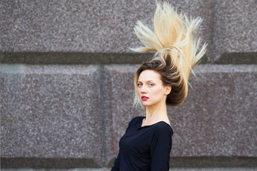 Sexy blonde girl in a black dress. With flying hair against a stone wall.