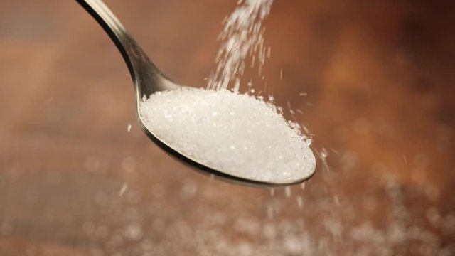 Stack of footage: White sugar fall through teaspoon down on a brown wood background. Slow motion. HD