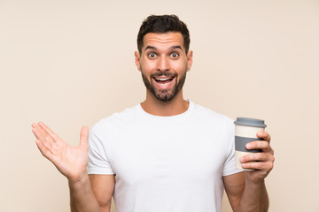 Young man with beard holding a take away coffee over isolated blue background with shocked facial expression