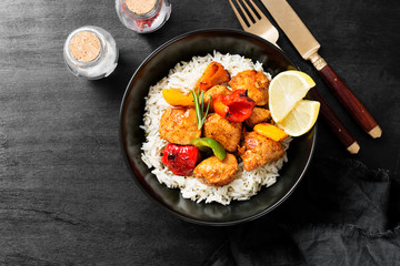 Grilled chicken breast and colorful peppers with fried rice on black background.