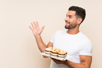 Handsome man holding muffin cake over isolated background with surprise facial expression