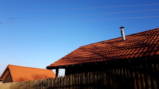 Fence made of sharp wooden stakes. Wooden houses with red tiled roof and blue clear sky. Sunny day