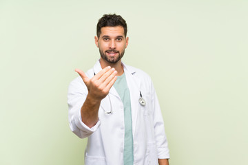 Young doctor man over isolated green wall inviting to come