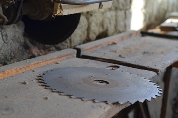 Old device for sawing wooden boards. A metal disc for sawing wood lies on a dusty work surface.