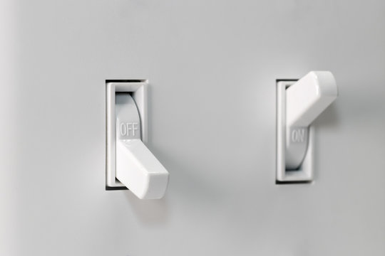 Closeup of white duplex light switch turned off and another turned on in background. Concept of energy saving, conservation