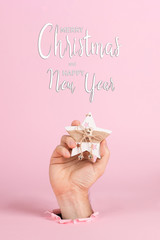 A male hand sticks out of a hole in pink paper, holds a Christmas tree ornament. Christmas concept symbol, commercial bucket print, copy space.
