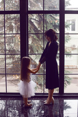 mother and daughter in dresses stand at a large window in the Studio