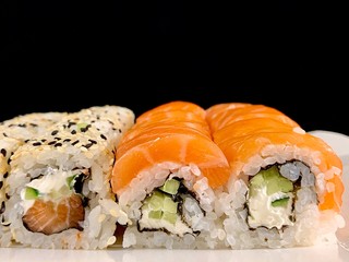 Sushi with red fish and avocado, close-up, on a black background. Japanese traditional cuisine, delicious sushi with dill and sesame seeds. Rolls - California and Philadelphia.